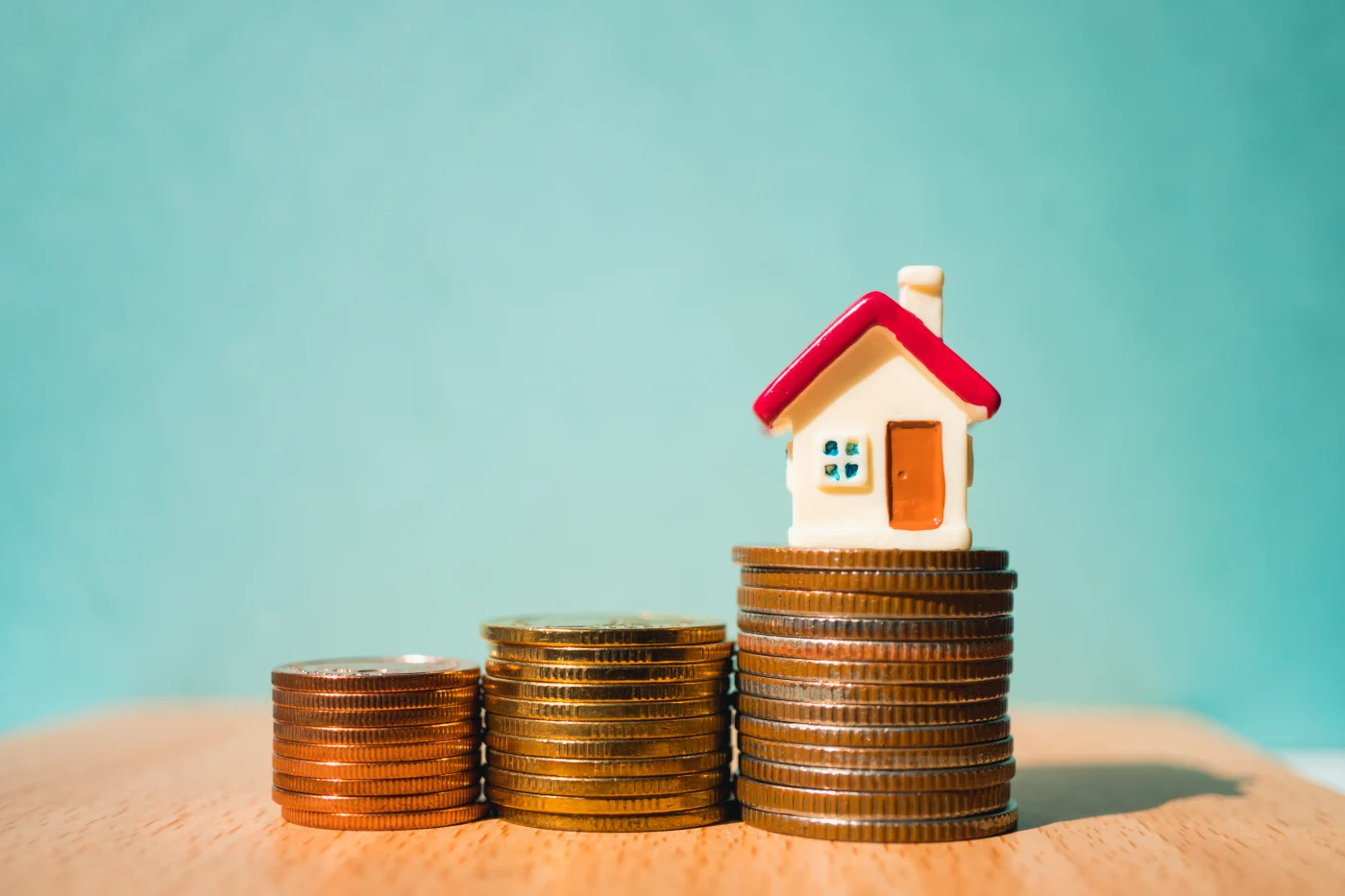 Stacks of coins on table with mini house on top