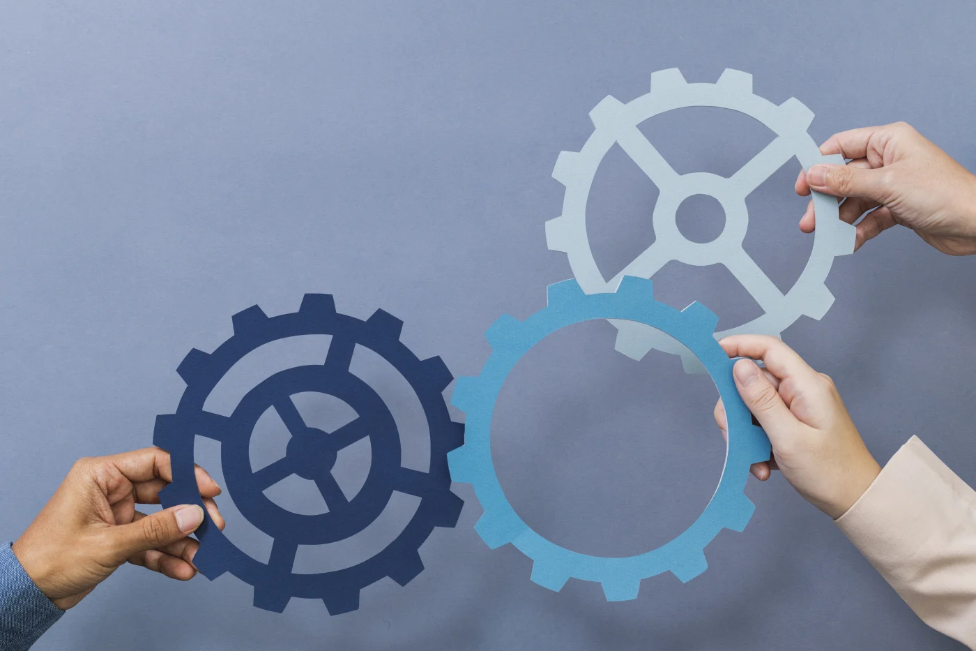 Three blue gears are held up and together by hands in front of blue background