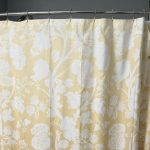 A “before” image of a traditional tub-and-shower setup in a South Shore Boston home. The space features a curved shower rod with a floral-patterned yellow and white curtain, light gray walls, and a metal towel rack. Though neat and functional, the setup lacks modern accessibility and visual appeal—setting the stage for a dramatic walk-in shower transformation.
