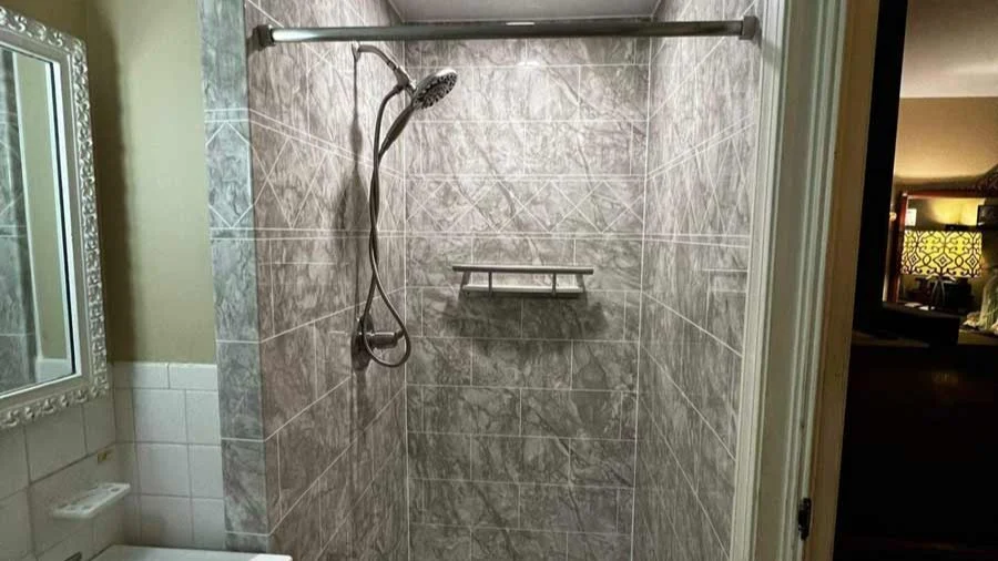 A newly remodeled walk-in shower with elegant gray marble-look tile and a clean, geometric layout. The shower features a modern handheld showerhead, built-in corner shelving, and polished metal fixtures. The crisp lines and luxurious tile pattern create a sleek, spa-like atmosphere—showcasing Bay State Bath’s craftsmanship and attention to detail.