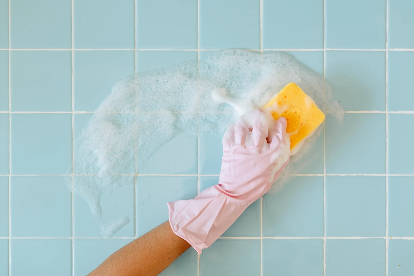 A Bay State Bath customer easily wipes a new light blue bath wall with sponge wearing pink gloves