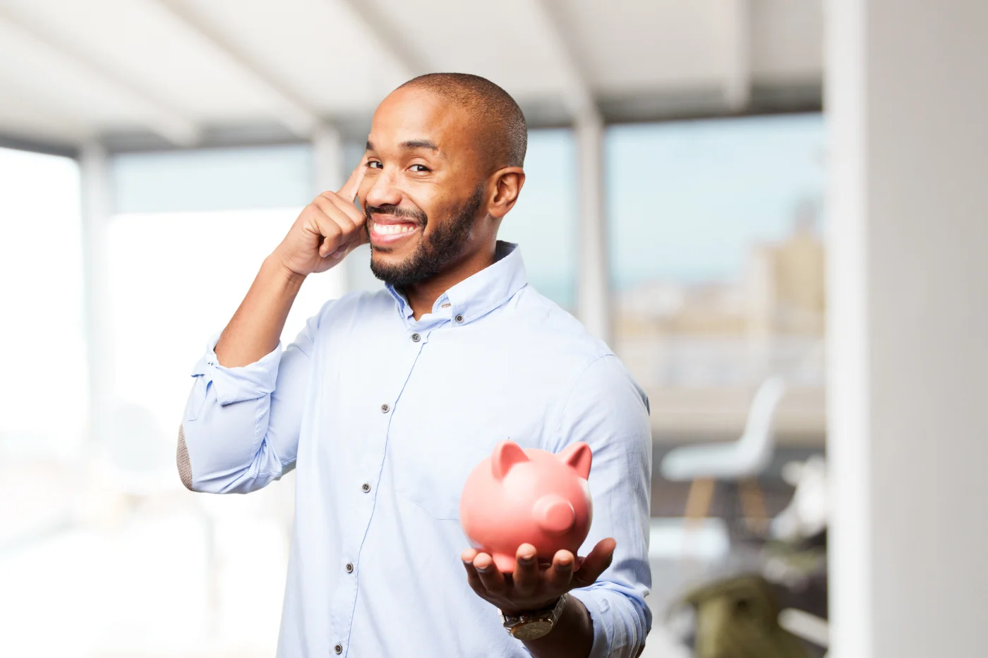 Man points to his head while holding piggybank toward camera