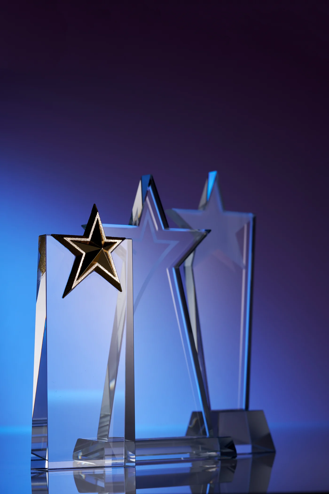 Three glass trophies with stars on top with dark blue background