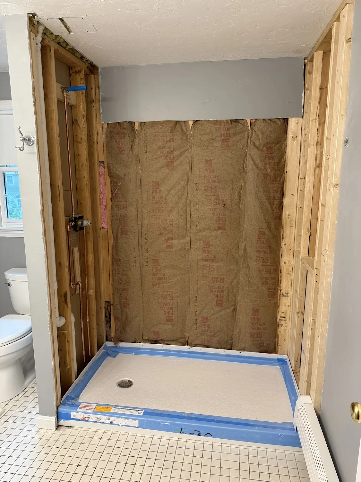 A partially completed bathroom remodel in South Shore Boston, showing the installation of a new walk-in shower pan. The walls have been stripped to the studs and insulated, with plumbing rerouted and visible. The newly installed shower base is protected with blue wrap, indicating it’s ready for the next phase. This photo highlights Bay State Bath’s precise prep work and layered project oversight.
