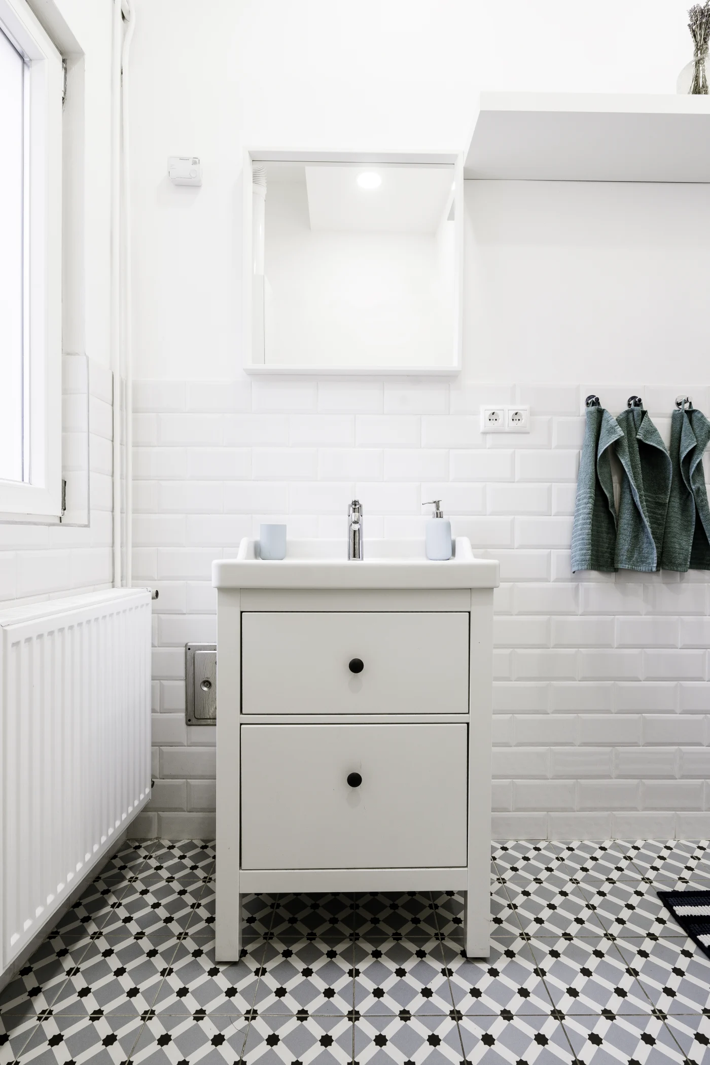 A minimalist bathroom with a white vanity and patterned black, white, and gray floor tiles with small print.
