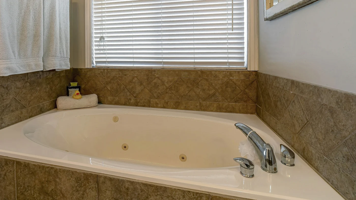 A brown bathtub wall surround with a white bathtub and silver features.