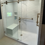 A white shower with a glass door, gold features, and a shower bench.