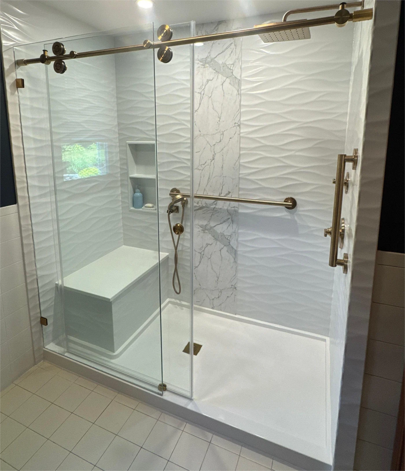 A white shower with a glass door, gold features, and a shower bench.