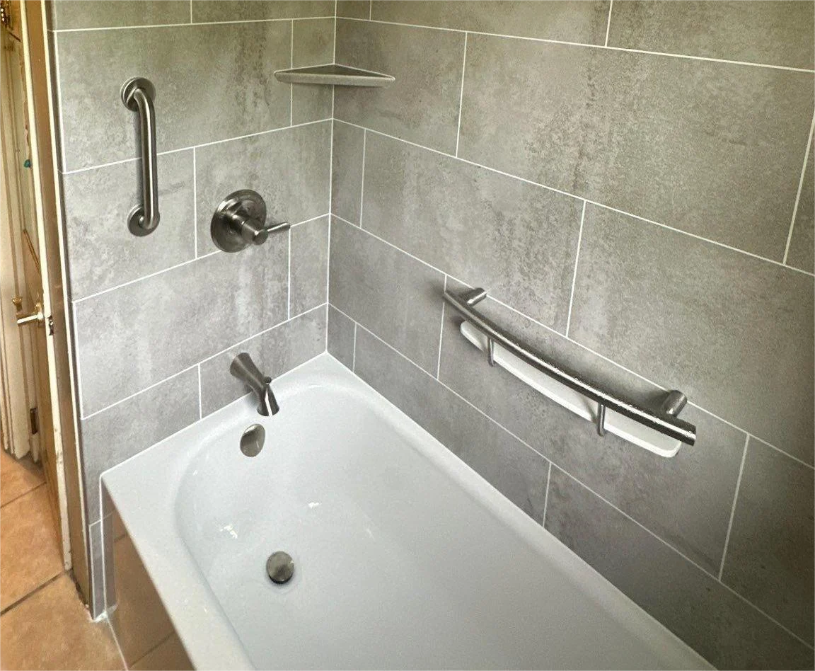 A white bathtub with silver features and a gray wall surround.