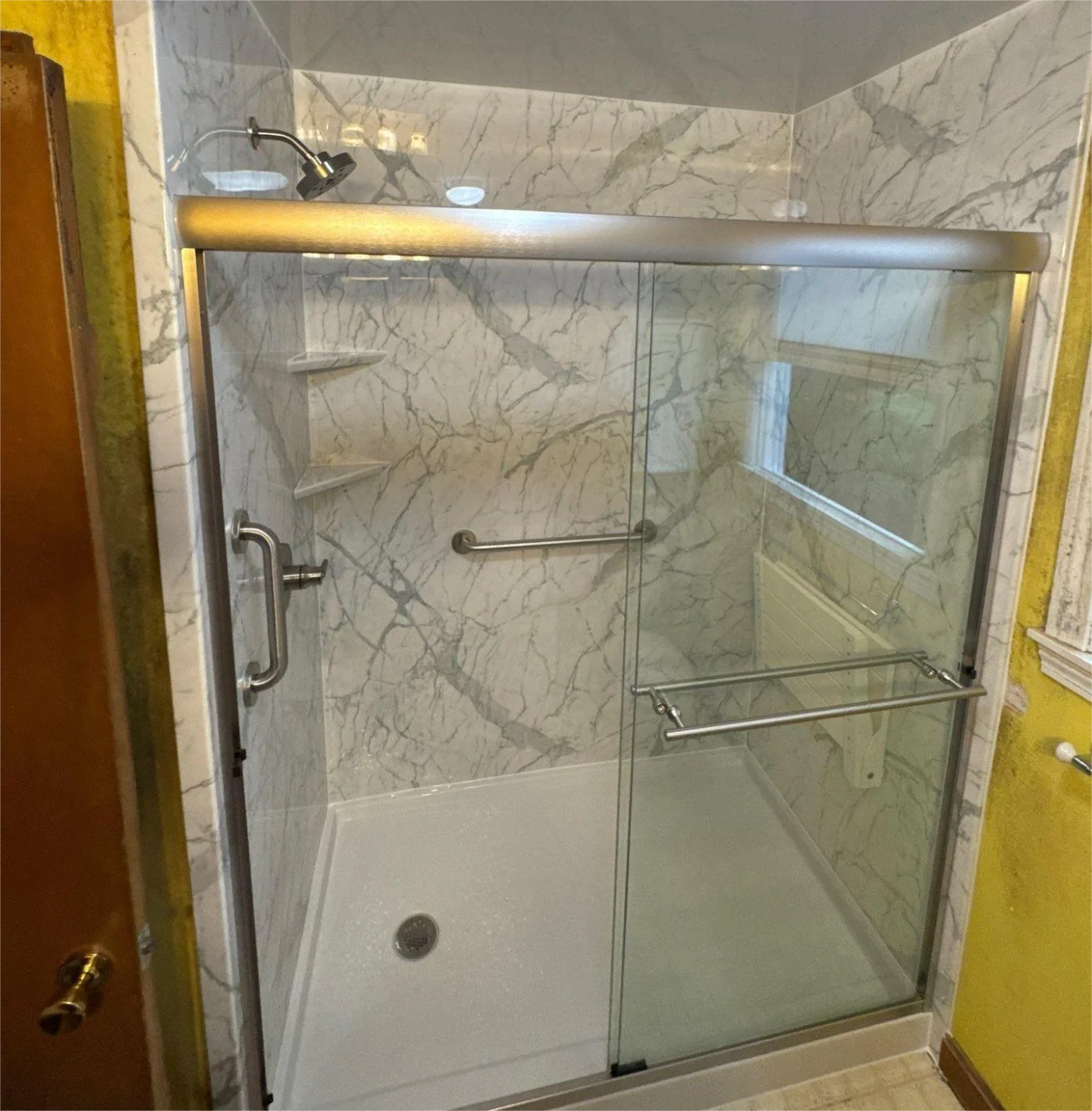 A walk-in shower with a glass door, silver features, white base, and gray wall.
