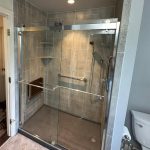 A walk-in shower with a glass door, grab rails, and silver features