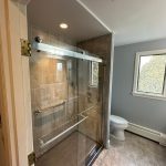 A walk-in shower with a glass door in a gray bathroom with tile floors.