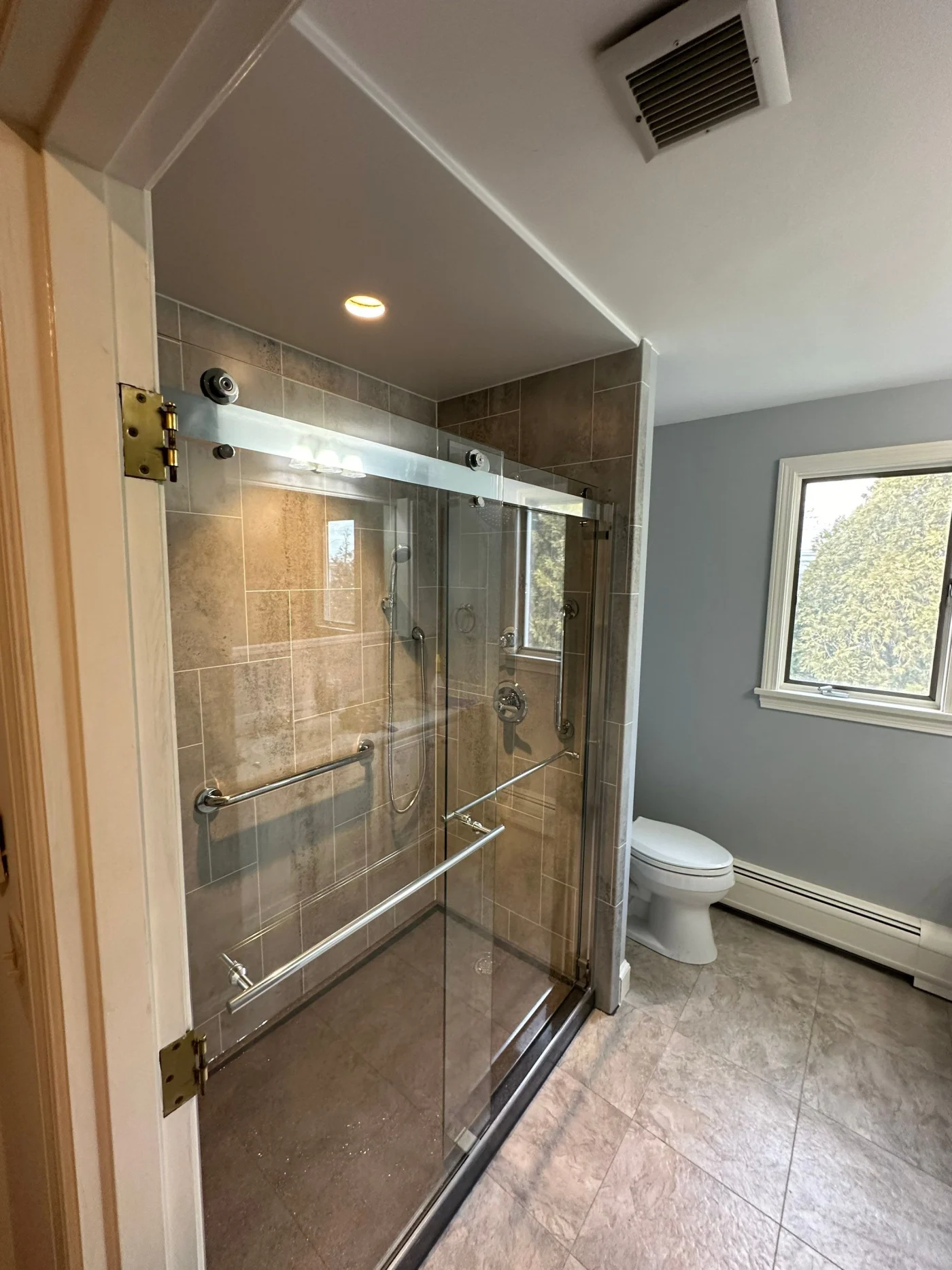 A walk-in shower with a glass door in a gray bathroom with tile floors.