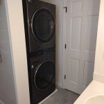 The view from the sink of a washer and dryer in the corner of a bathroom.