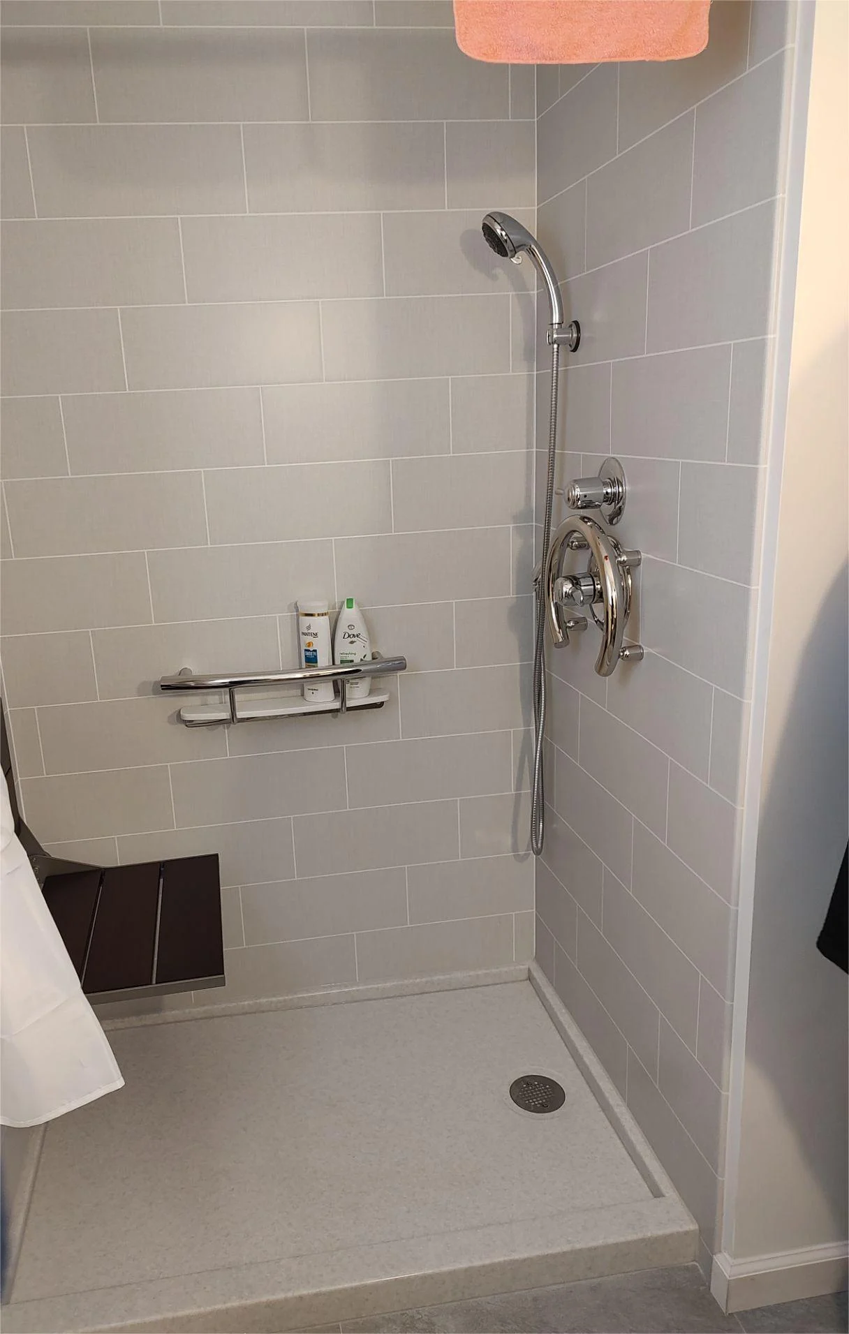 A gray walk-in shower with a gray base, silver fixtures, and a wooden seat.
