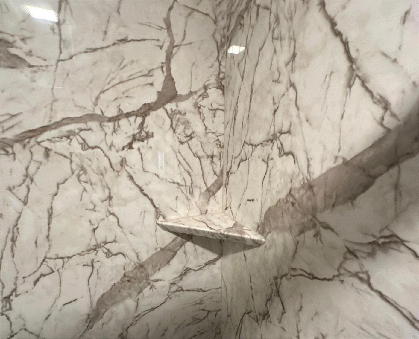 A close-up of the corner of a white and gray bathtub wall with a built-in shelf.