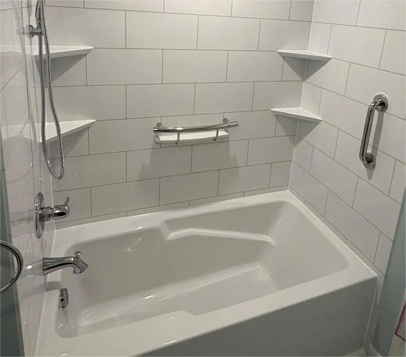 A white bathtub with silver fixtures, built-in shelves, and a white wall.