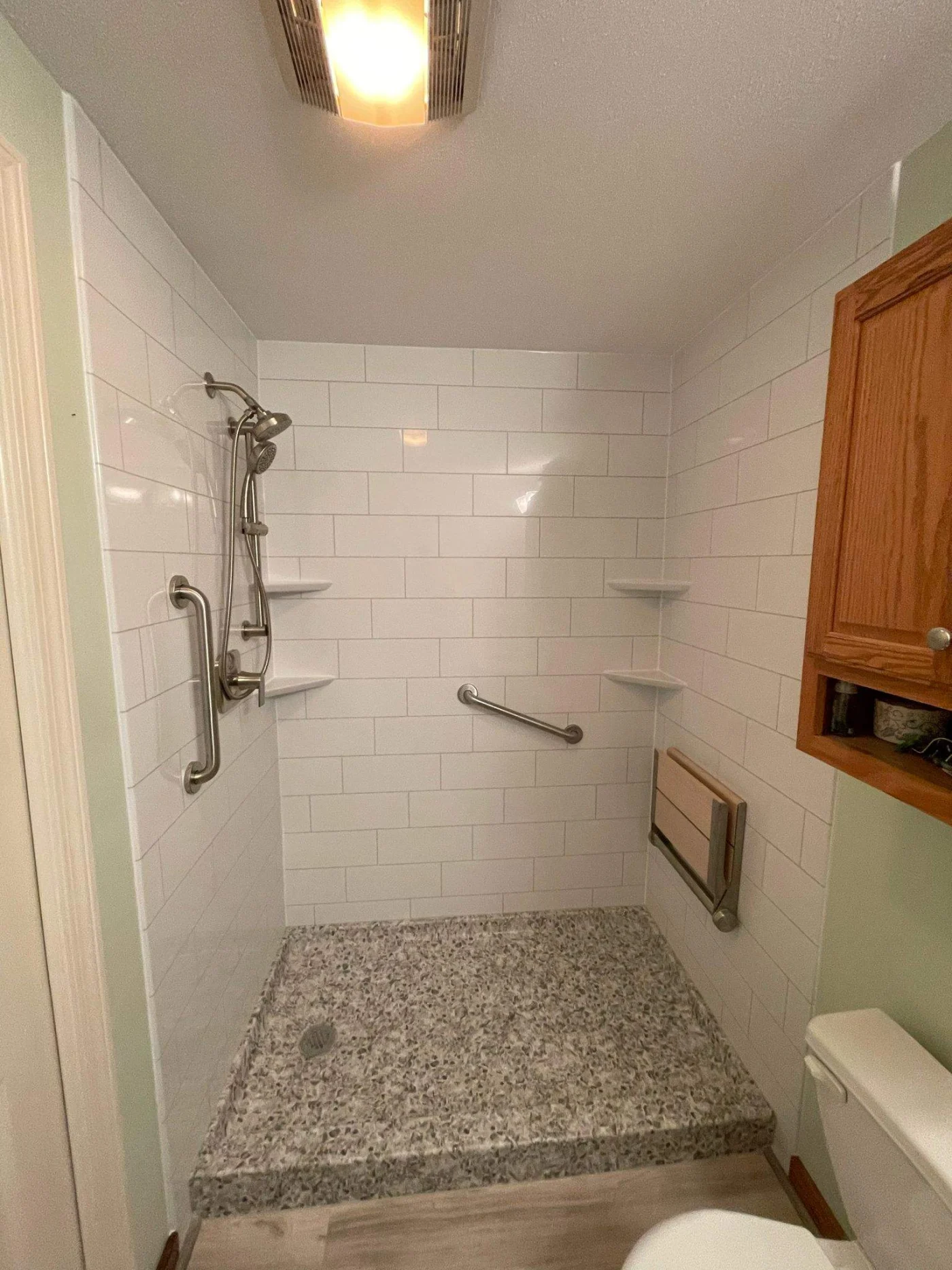 A white walk-in shower with silver fixtures, a seat, built-in shelves, and a gray base.