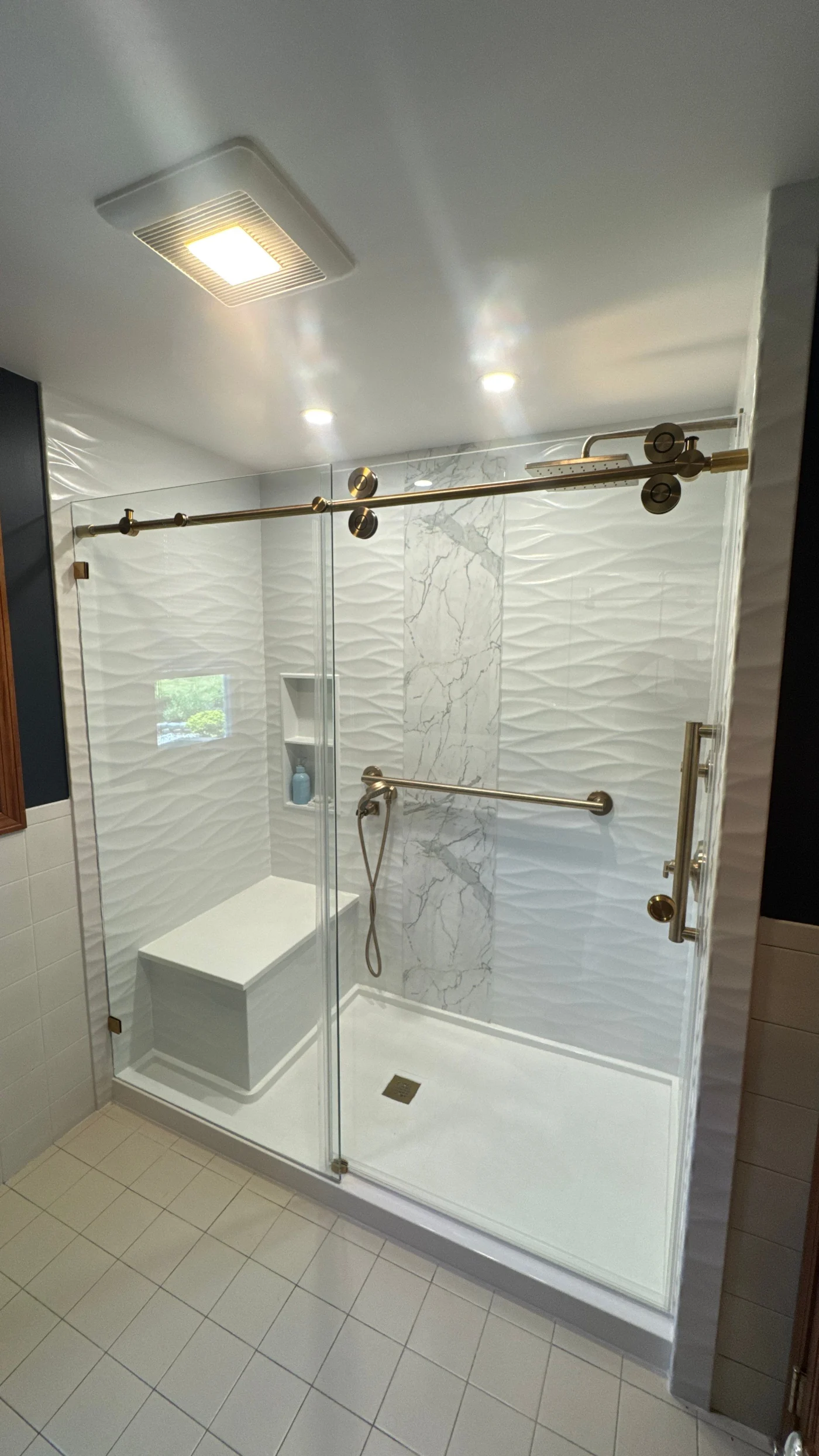 A white walk-in shower with gold fixtures, a bench, and a glass door.