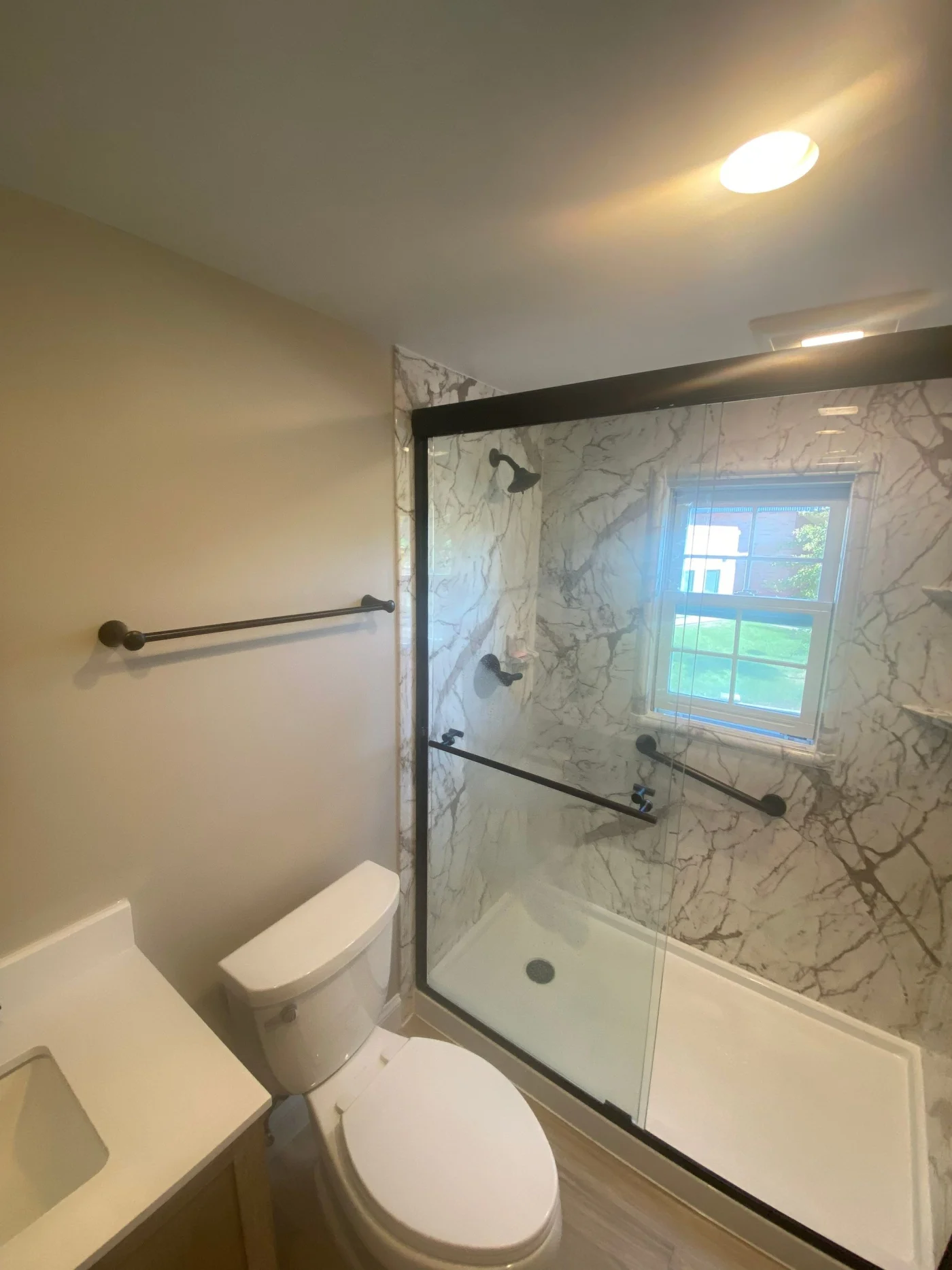 A tan bathroom with a white toilet and a gray walk-in shower with black fixtures, a white base, and a sliding glass door.
