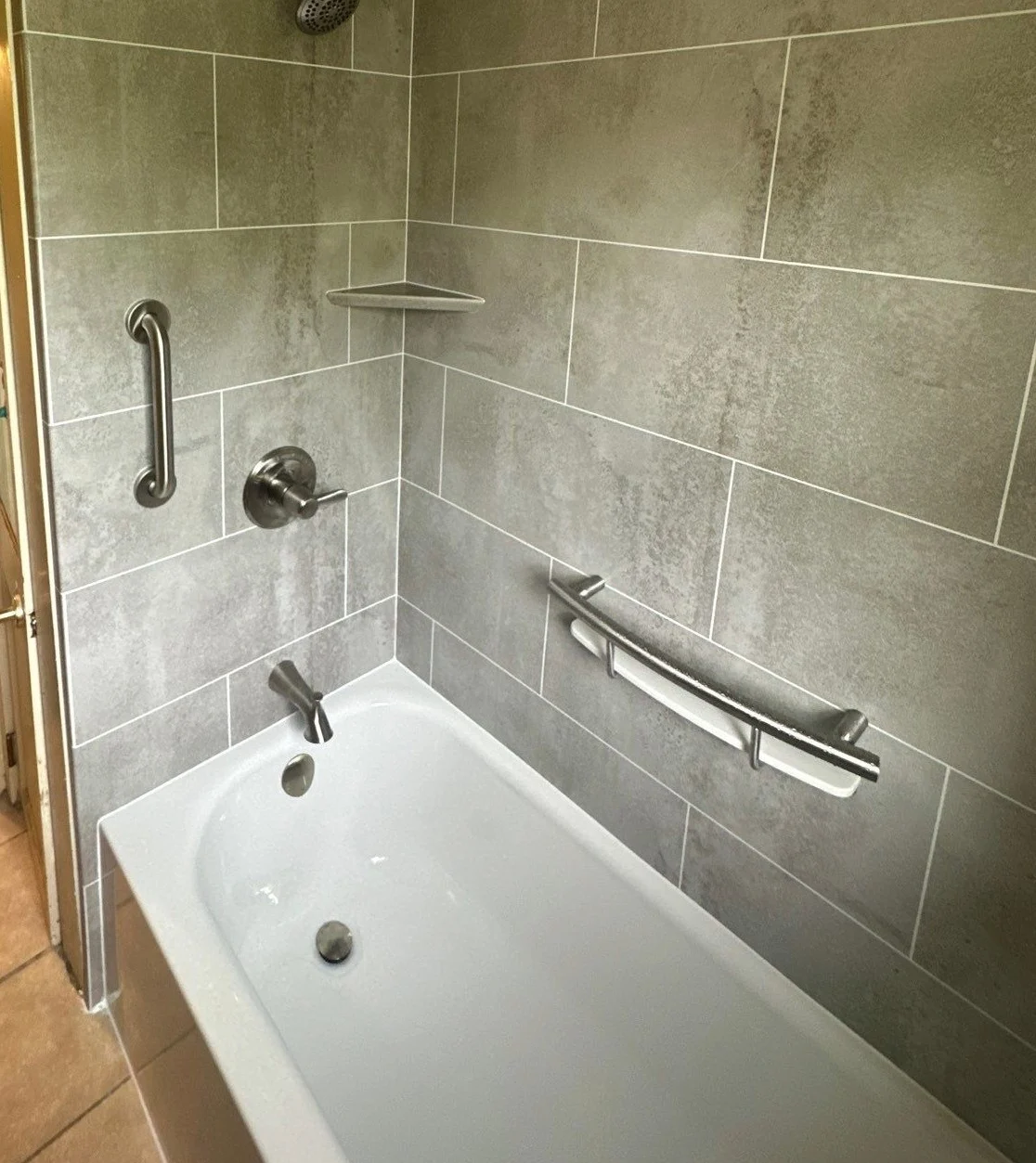 A white bathtub with gray walls, silver fixtures, and built-in shelves.