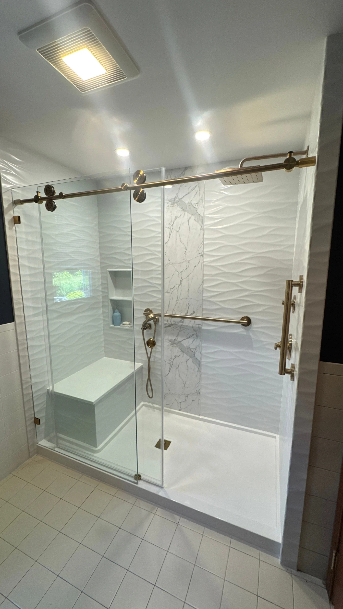 A white walk-in shower with a bench, gold fixtures, and a sliding glass door.
