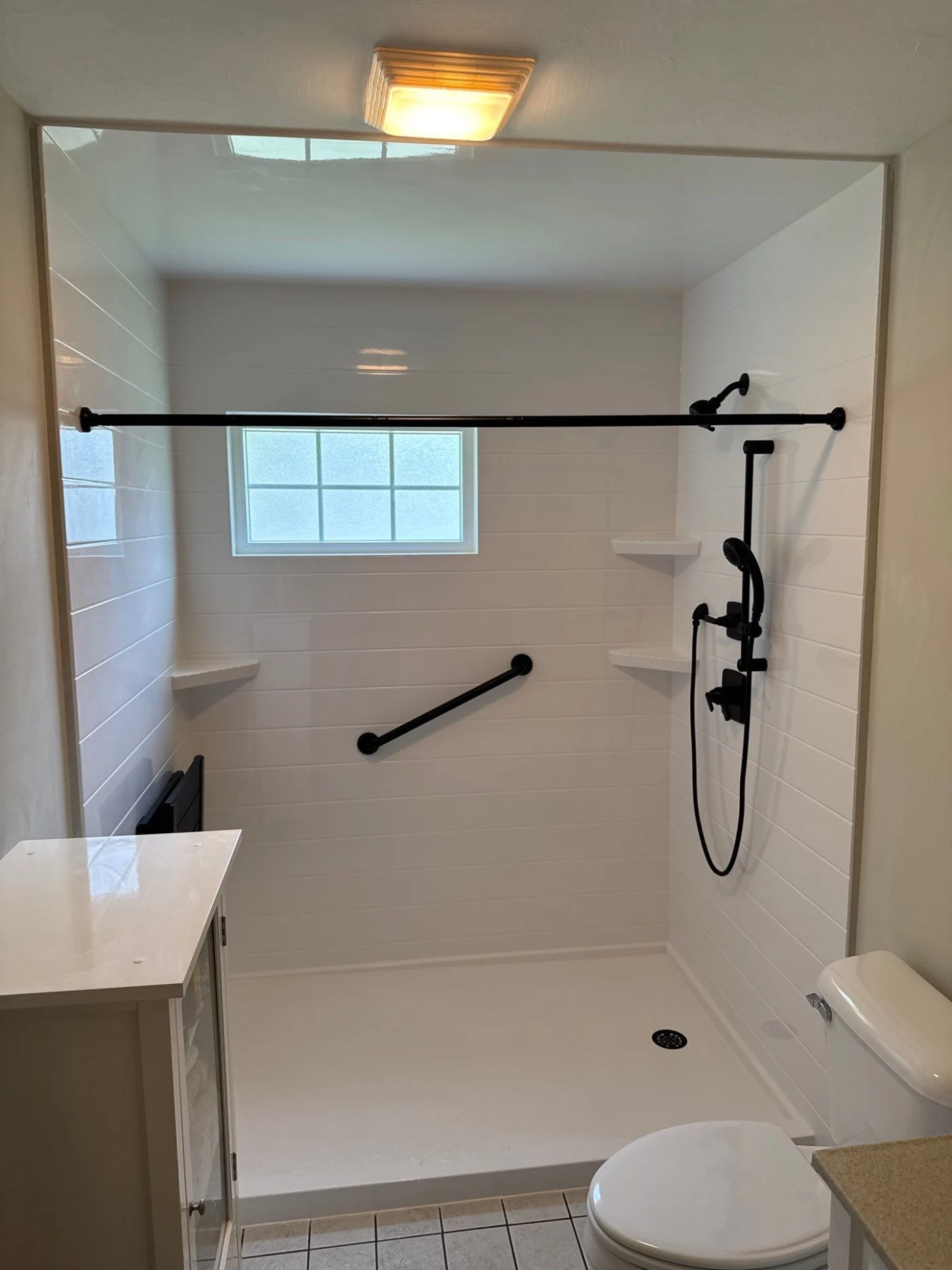 A white walk-in shower with black fixtures, built-in shelves, and a window.