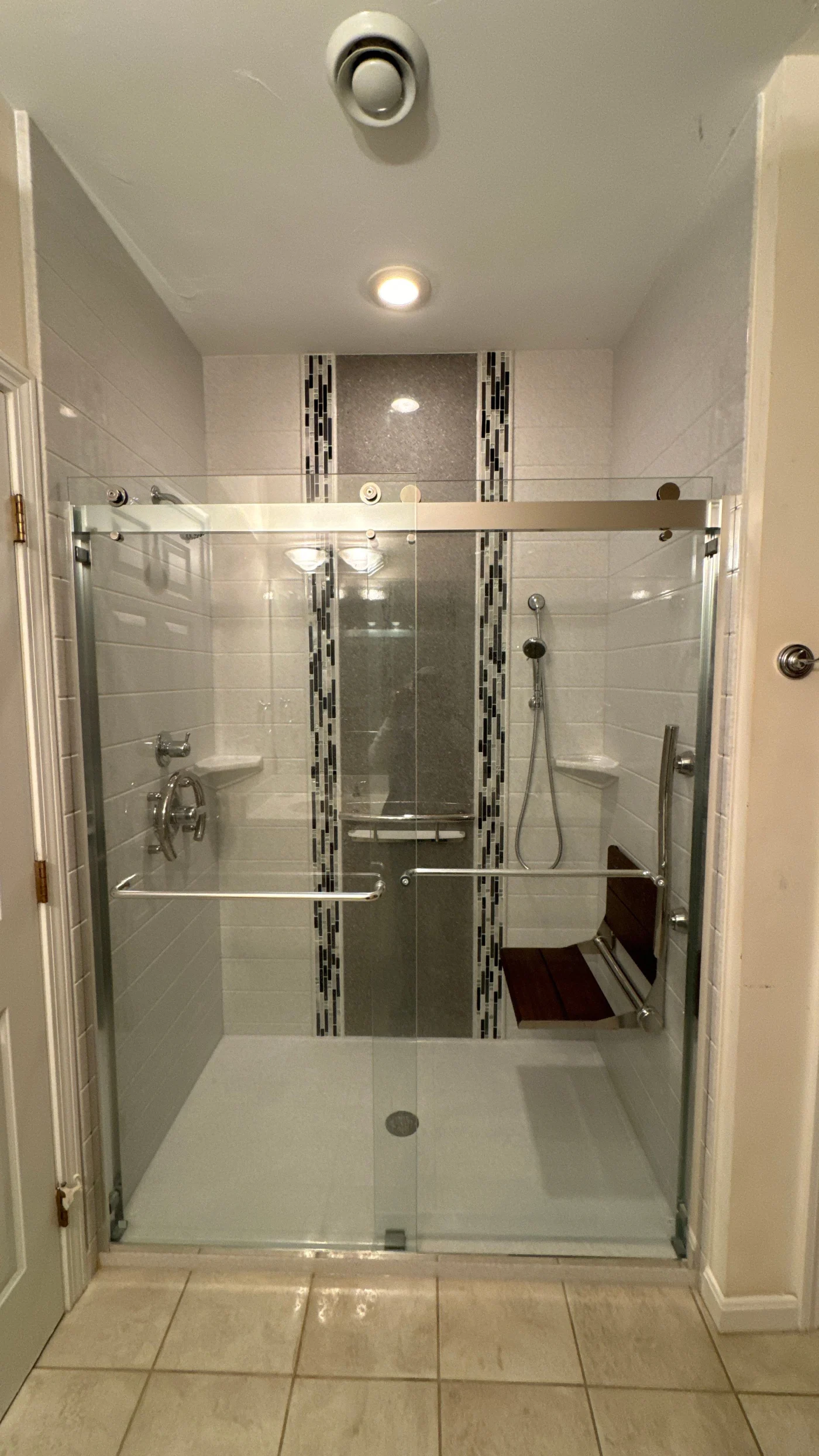 A white and gray walk-in shower with silver fixtures, a seat, and a glass door.
