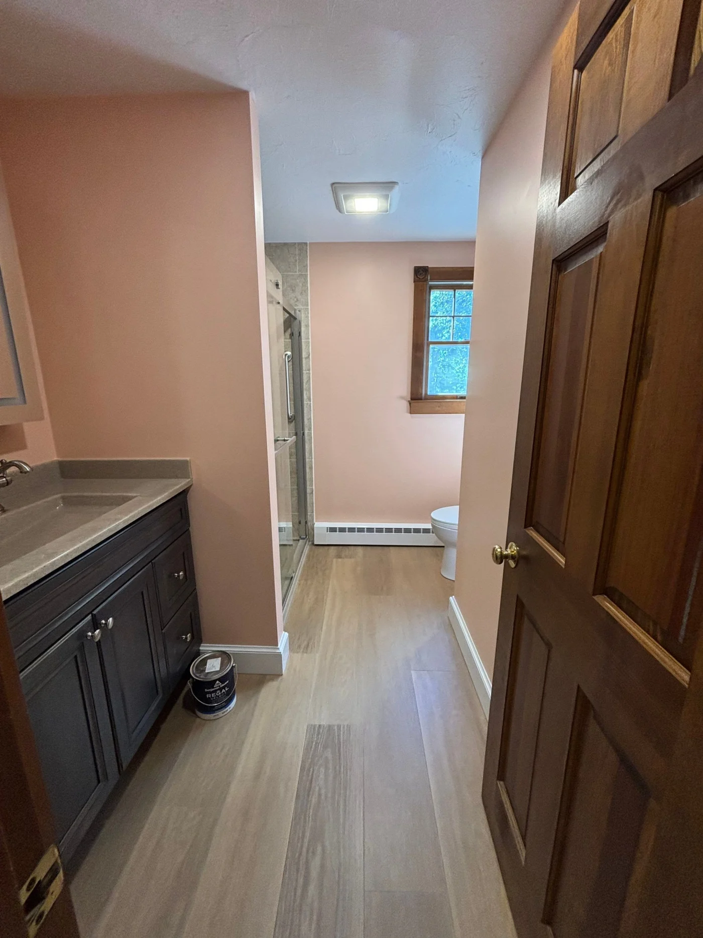 A pink bathroom with a black vanity, gray countertop, linoleum flooring, and a walk-in shower.