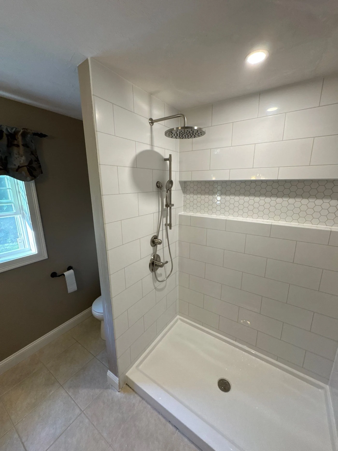 A white walk-in shower with silver fixtures and a white base.
