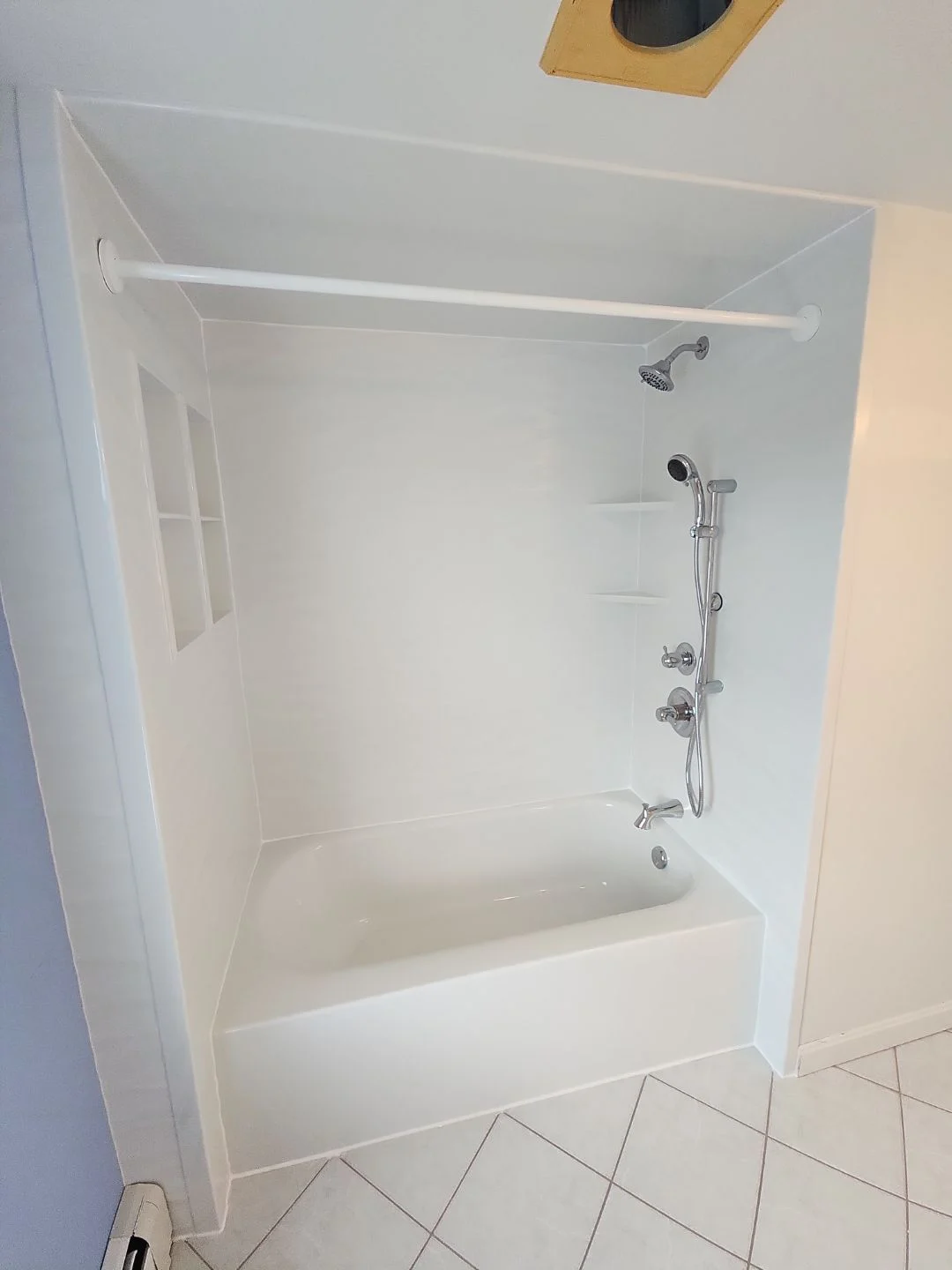 A white bathtub with white walls, built-in shelves, and silver fixtures in a white bathroom.