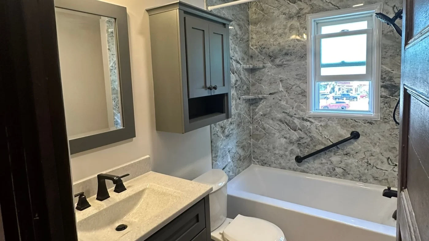Elite Bathroom Remodeling | Boston, MA | Bay State Bath Remodeled bathroom with a white bathtub, marble-look shower walls, gray vanity, and black fixtures.