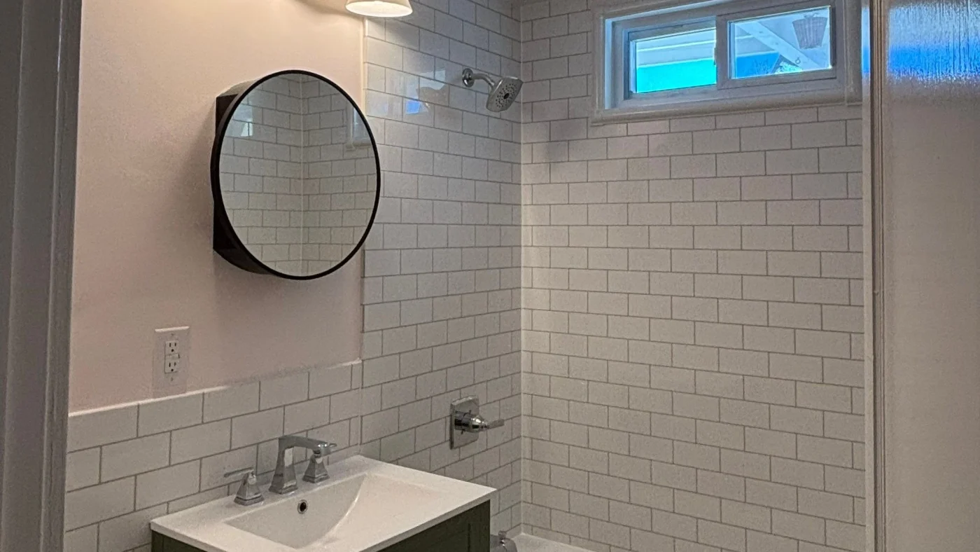Remodeled bathroom with white subway tile walls, a walk-in shower, dark vanity, and round mirror.