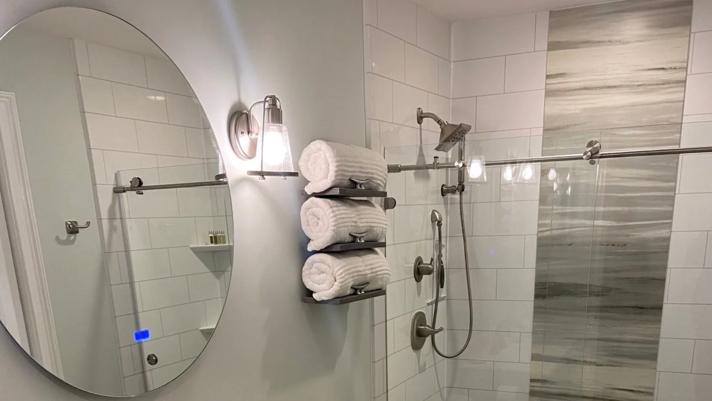Modern glass-enclosed shower with white tile walls, decorative accent panel, rainfall showerhead, and handheld showerhead.