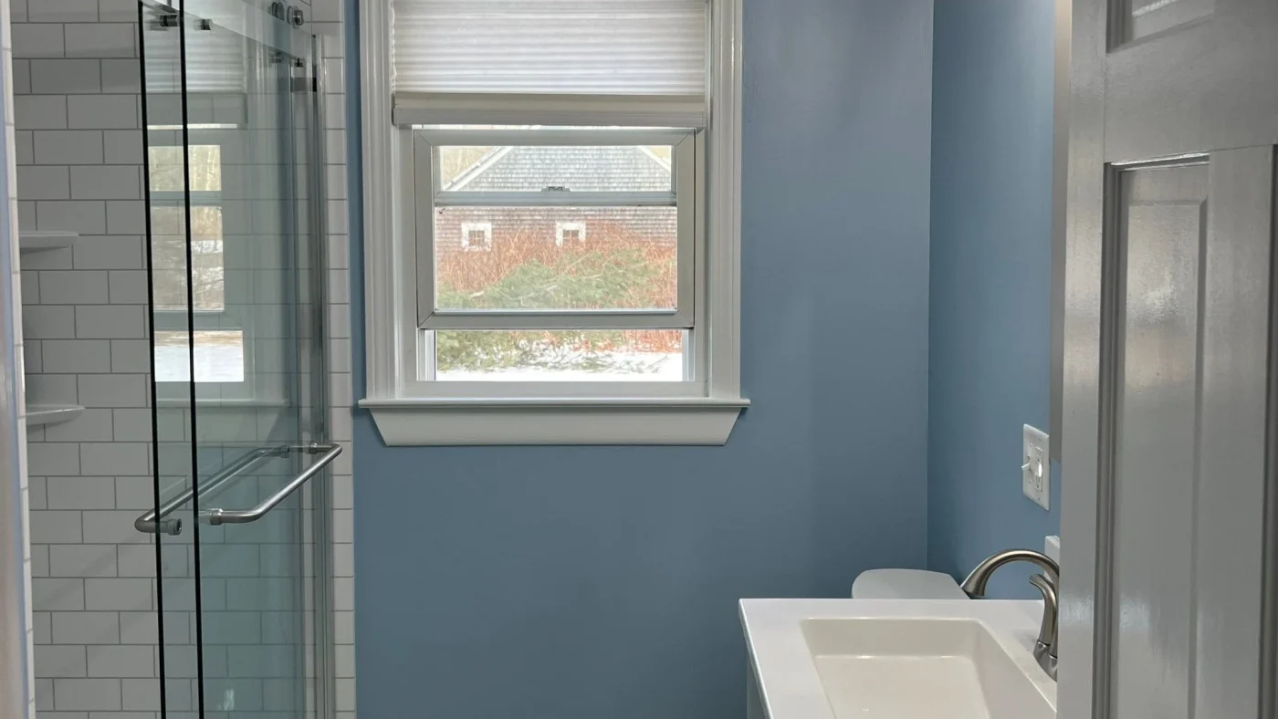 Remodeled bathroom with blue walls, a glass-enclosed white tile shower, and a white vanity.