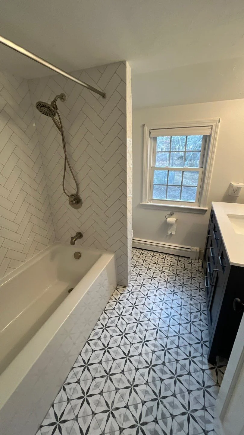 This pristine bathroom remodel features a low-threshold walk-in shower with crisp white vertical subway tiles, sleek matte black fixtures, a built-in safety grab bar, and a matching corner shelf unit.