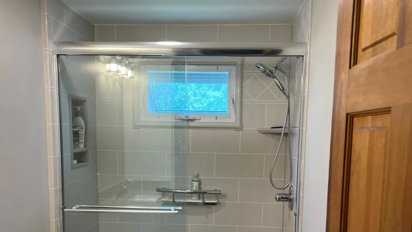 Walk-in shower with gray tile walls, sliding glass doors, built-in niches, and a handheld showerhead.