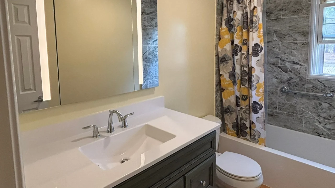 Remodeled bathroom with a white vanity, bathtub, marble-look wall surround, and floral shower curtain.