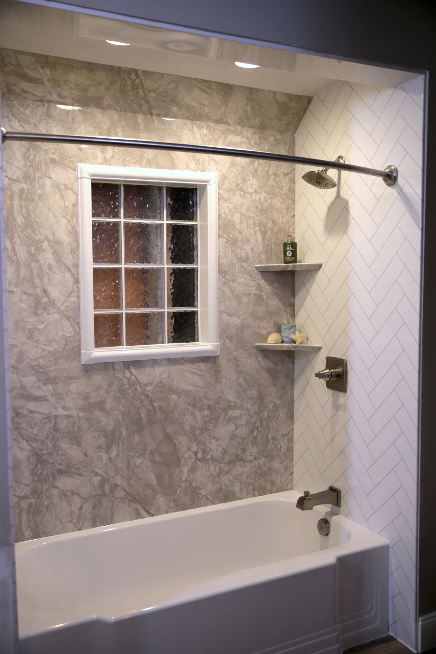 A white bathtub with silver fixtures, built-in shelves, white and gray walls, and a window.