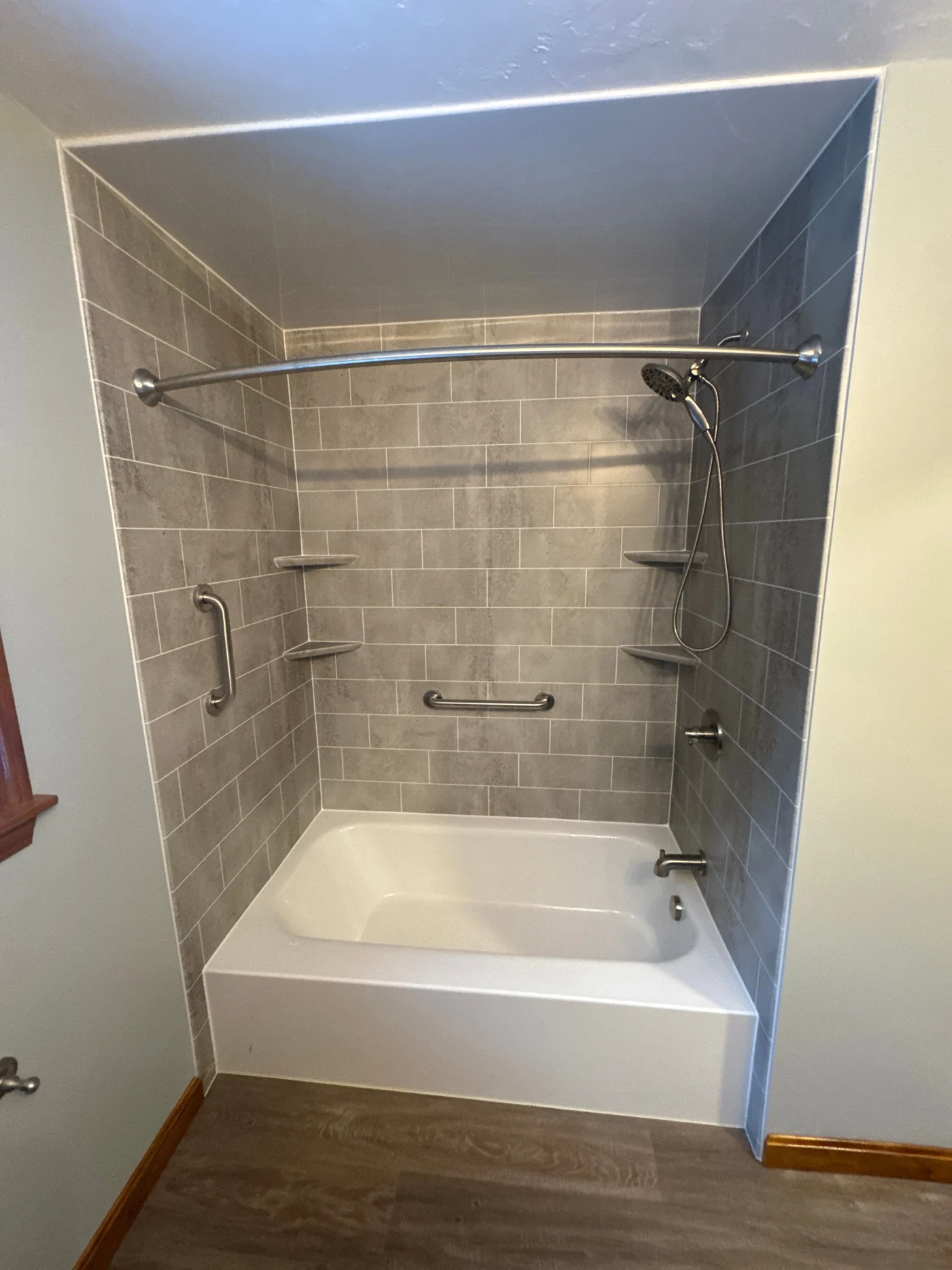 A white bathtub with gray walls, silver fixtures, and built-in shelves.