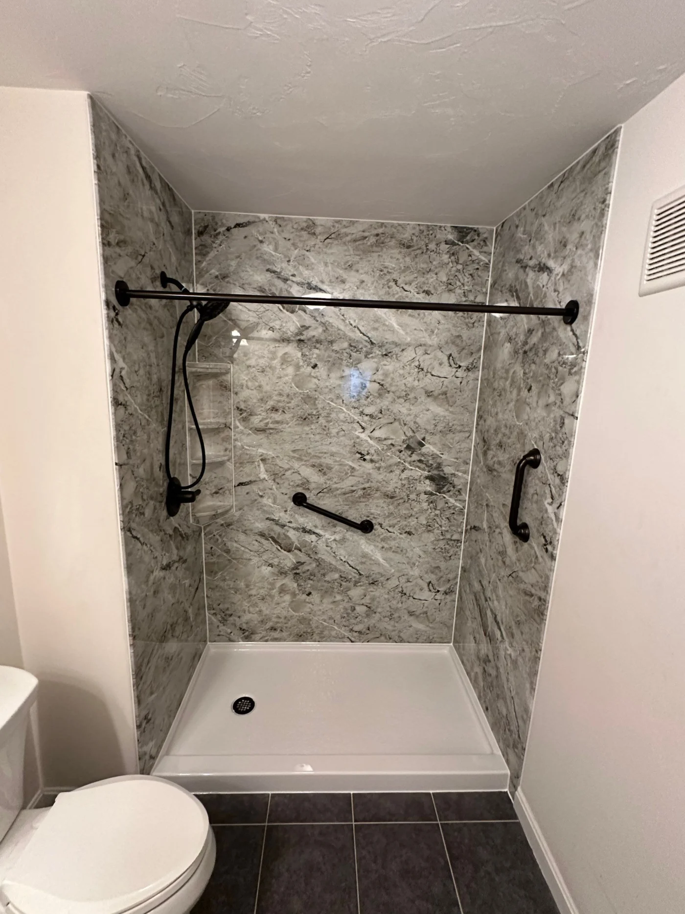 A walk-in shower with a white base, a gray surround, and black fixtures.