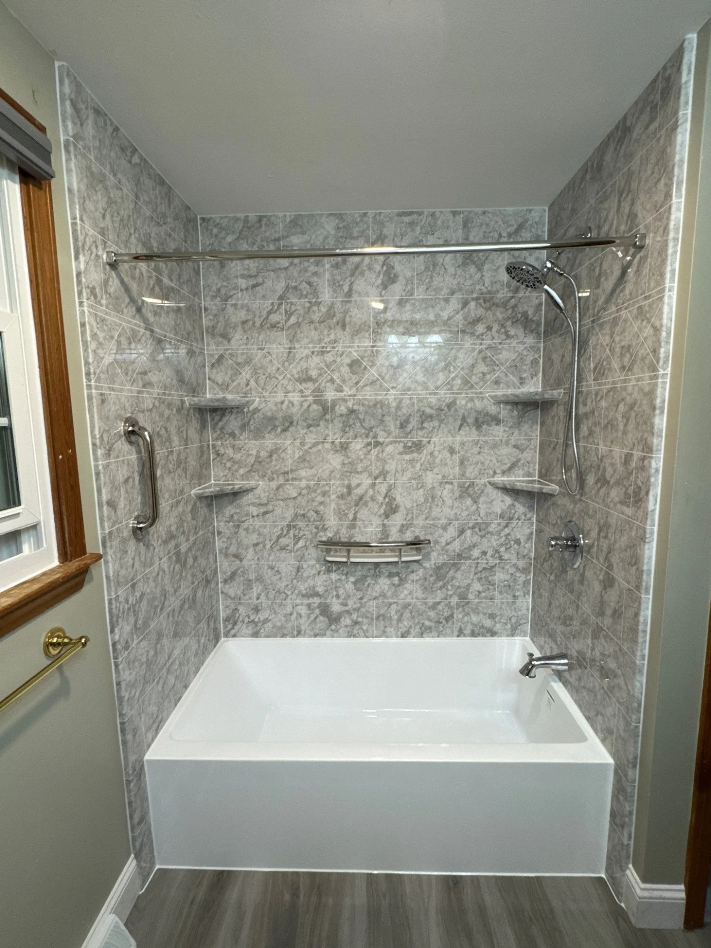 A crisp white alcove bathtub features integrated gray marbled tile walls with a diamond-patterned accent trim, multiple corner shelves, chrome grab bars, and a straight shower rod.