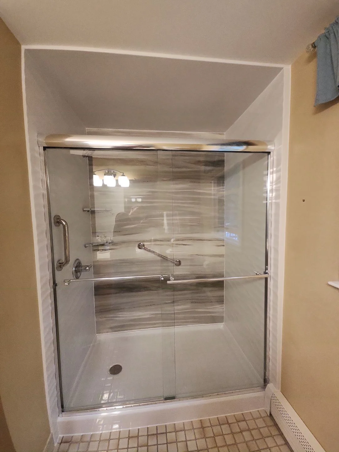 A walk-in shower with gray and white walls, a white base, silver fixtures, and a sliding glass door.