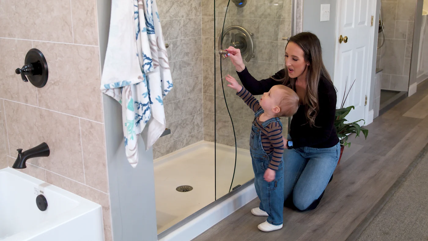Baby Riche inspects glass shower door inside the Bay State Bath showroom with his mom