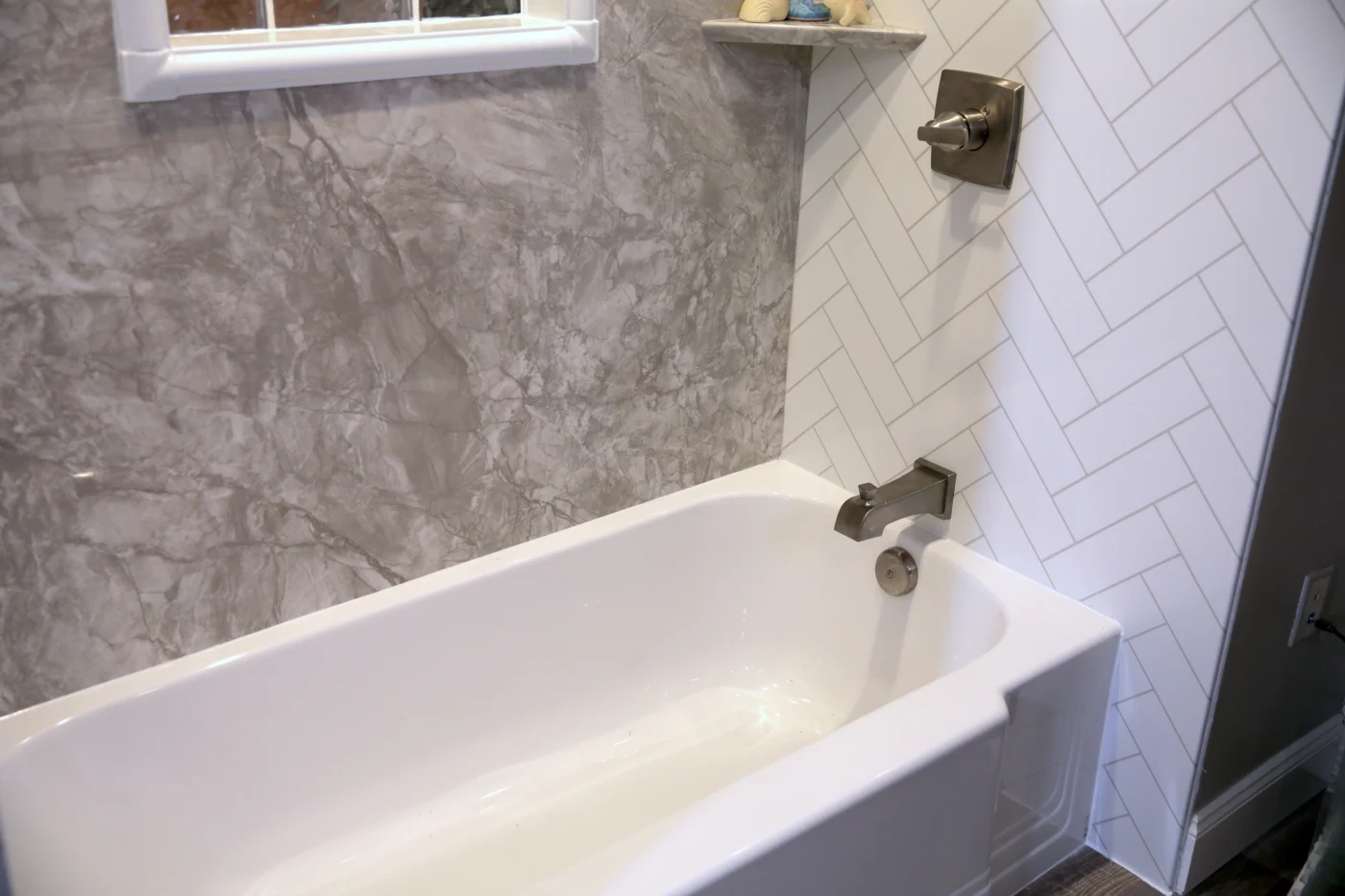 A white bathtub with a silver faucet and handle with a gray side wall and a white wall behind the faucet.