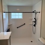 A white walk-in shower with black fixtures, white shelves, a white base, and a window.