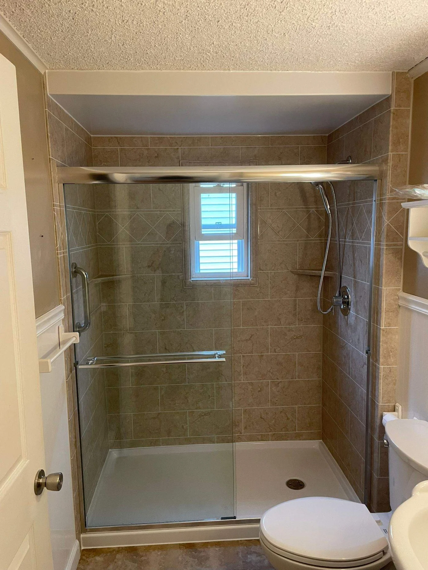 Secure Shower Base & Wall Installation In Kingston, MA | Bay State Bath A walk-in shower with brown tile walls, a white base, silver fixtures, and a sliding glass door.