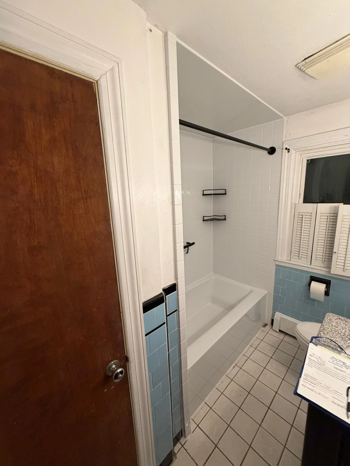 A refreshed alcove bathtub features bright white tile-look bathtub wall surrounds paired with built-in storage shelves and dark hardware accents.