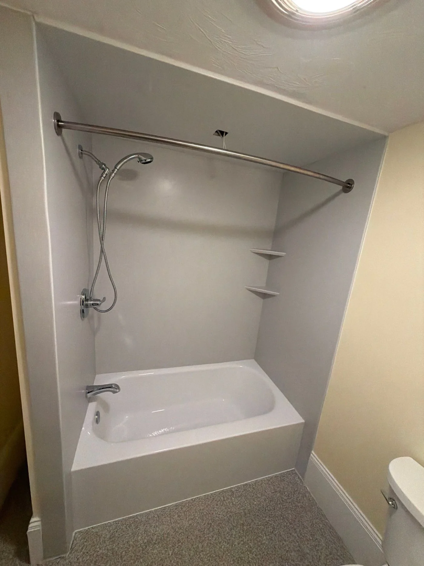 An updated alcove bathtub setup features clean, solid grey bathtub wall surrounds equipped with corner storage shelves and a handheld showerhead.