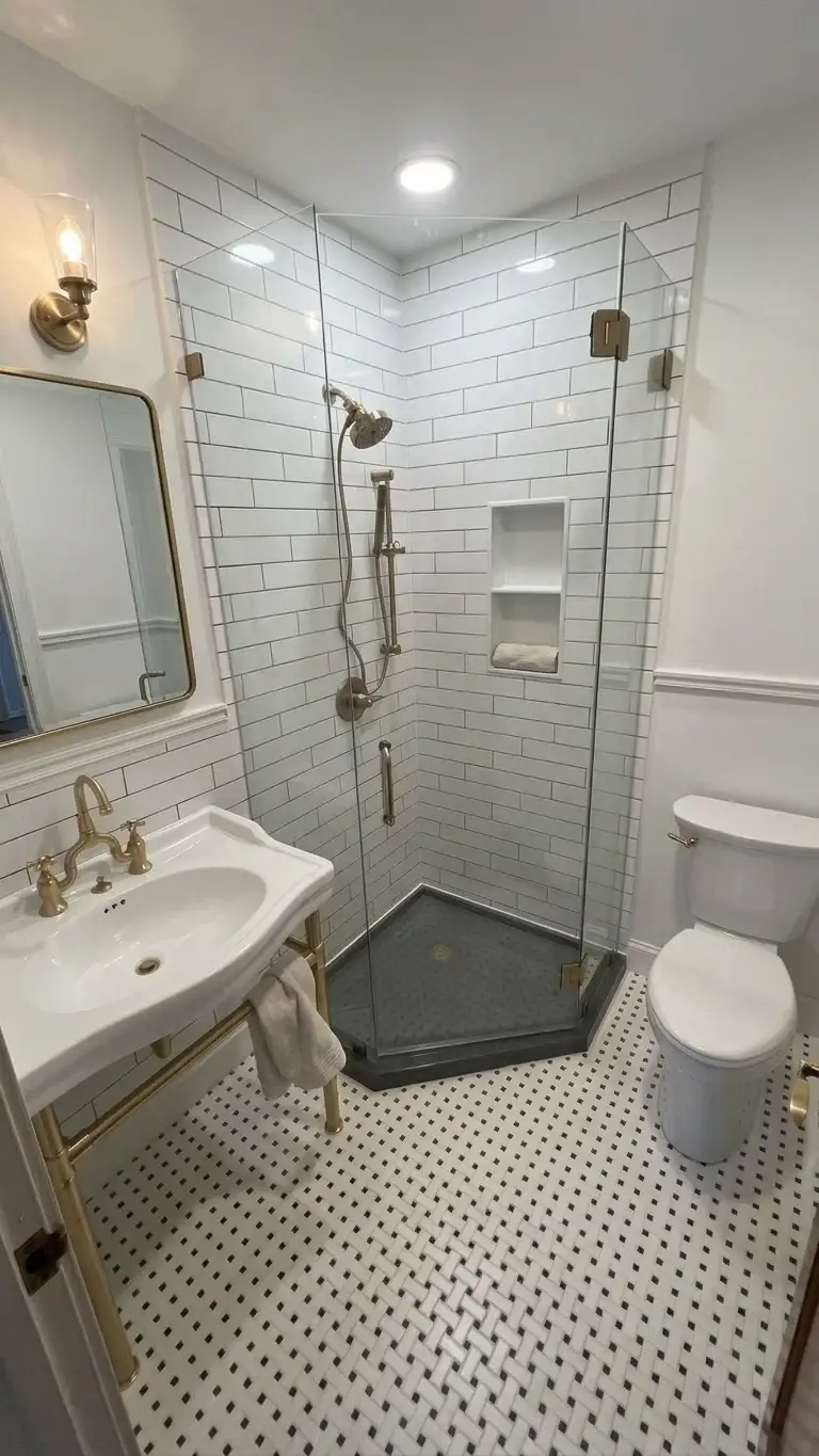 An elegant full bathroom remodel features classic mosaic floor tile, brushed brass fixtures, a console sink, and a glass-enclosed corner shower with white subway wall tile.